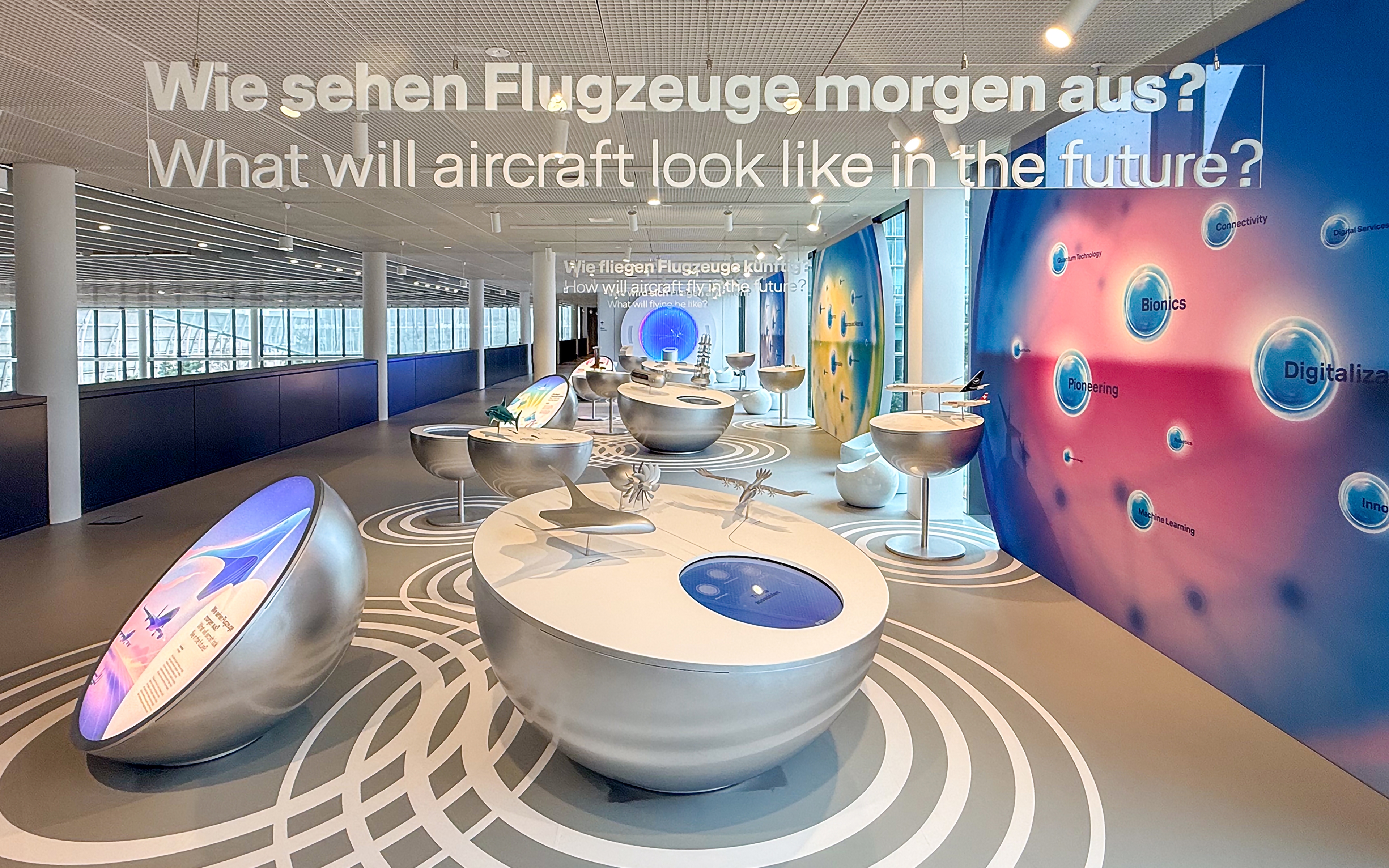 Lufthansa exhibition space about future aviation, with interactive displays, aircraft models, and large wall graphics asking “What will aircraft look like in the future?”
