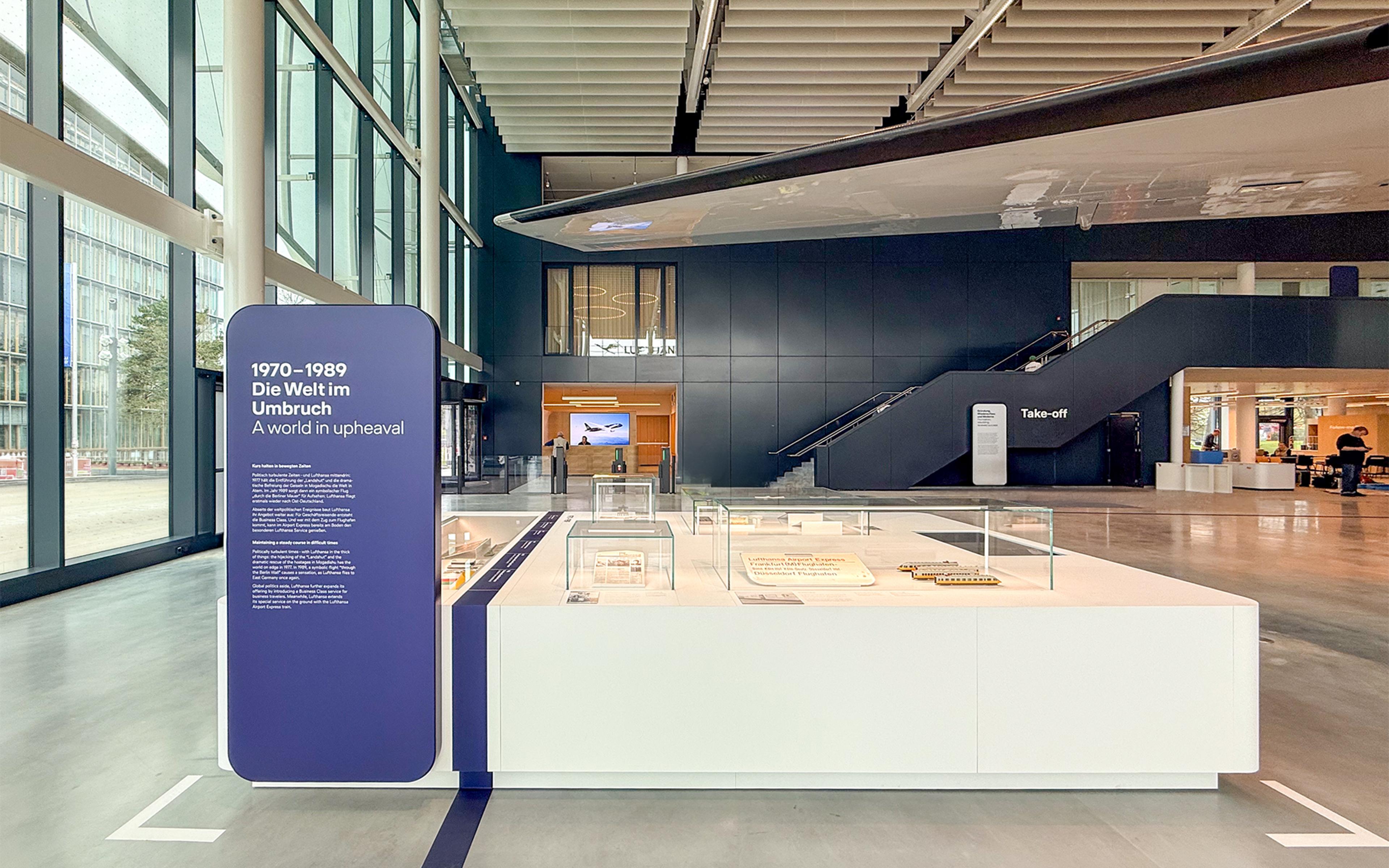 Spacious Hangar One hall with a suspended airplane wing, display cases, and a large sign reading “1970–1989: A world in upheaval,” exploring aviation history.