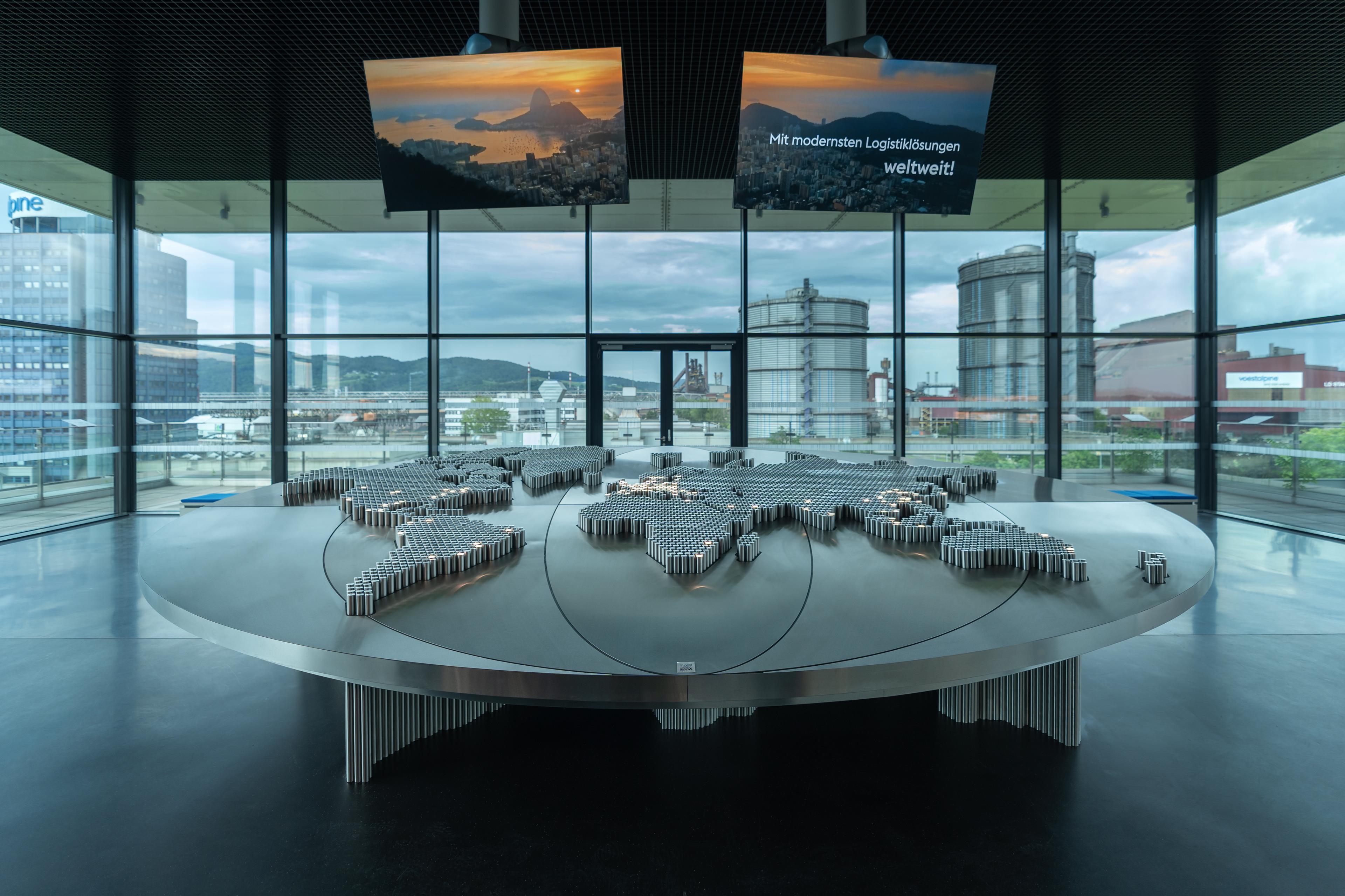 Interactive world map made of steel cylinders inside the voestalpine Stahlwelt, set against panoramic views of the industrial site and displaying the company’s global presence