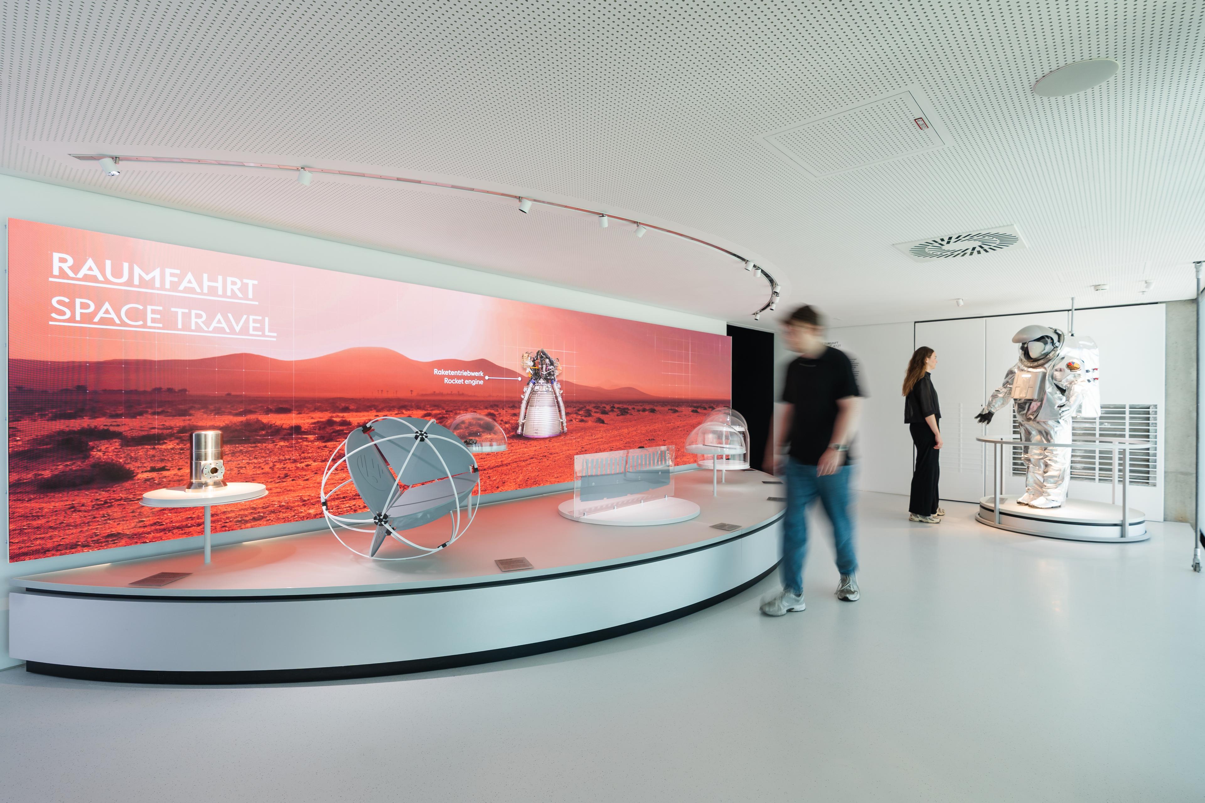 Space technology exhibition featuring aerospace components, a life-size astronaut suit, and immersive media displays exploring future applications of high-performance steel