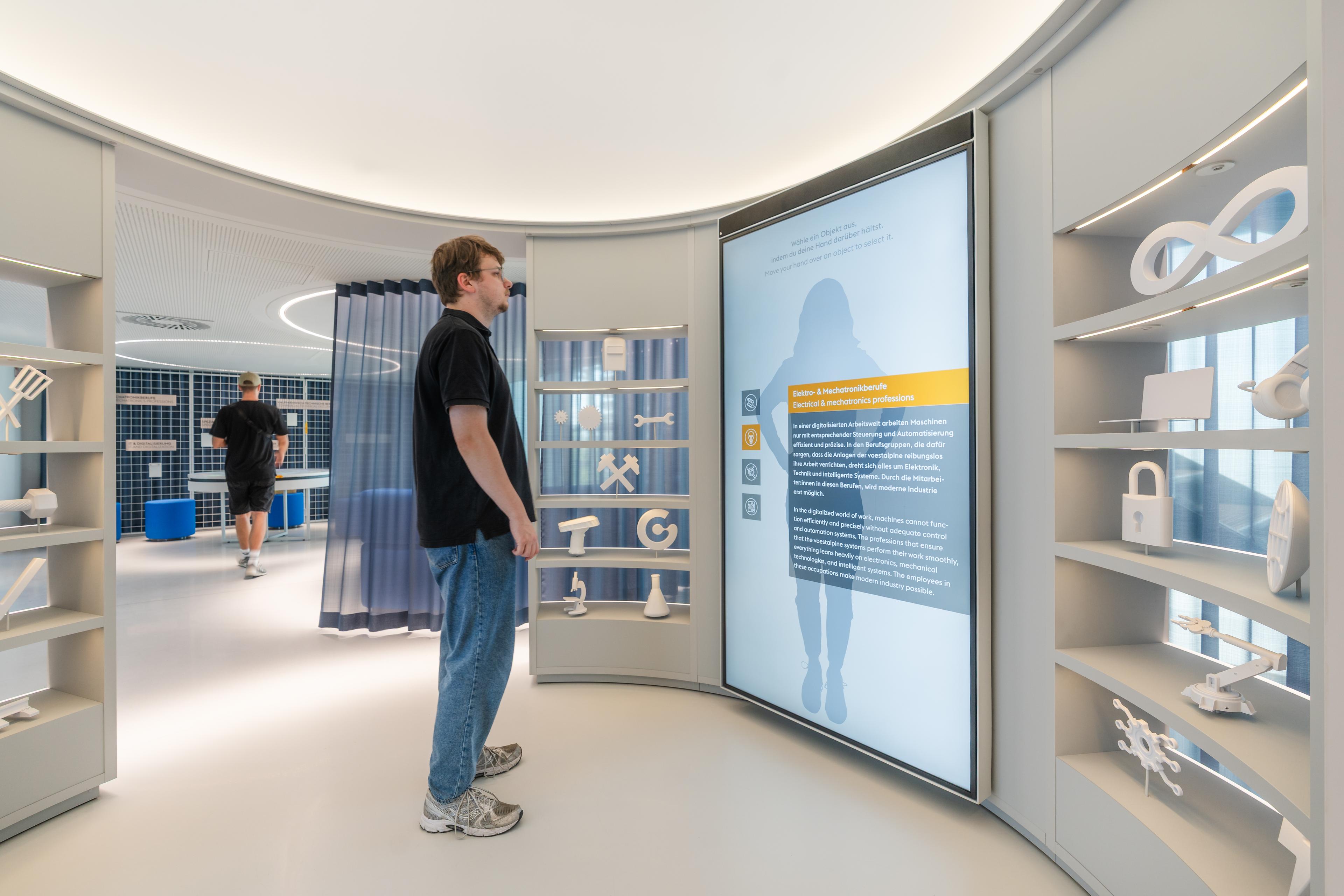 Visitor interacts with a digital exhibit exploring career paths at voestalpine, surrounded by symbolic objects and multimedia content about the company’s working world
