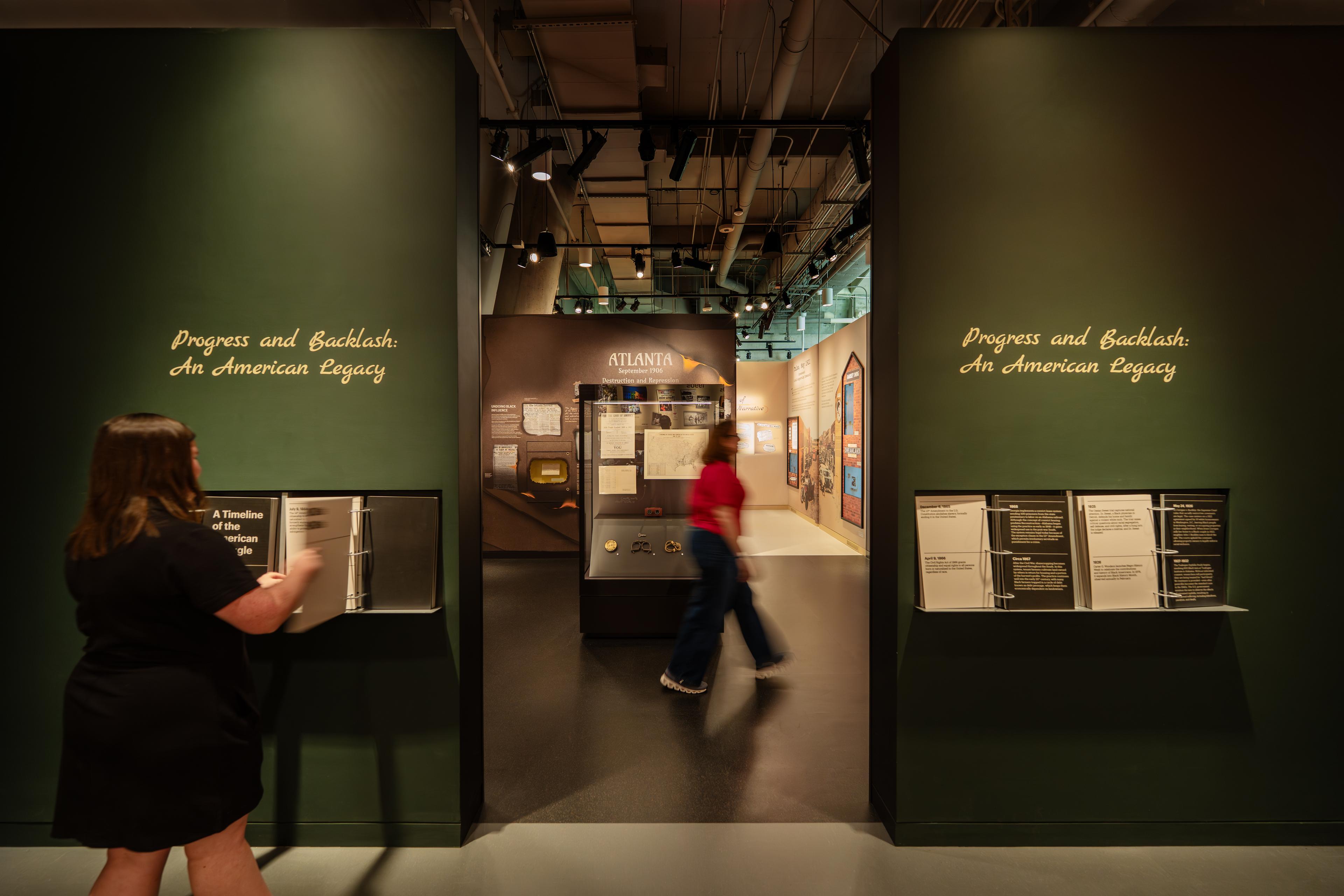 Entrance to the section “Progress and Backlash: An American Legacy.” Two dark-green walls frame a gallery filled with historical documents, photographs, and interpretive displays. Visitors engage with introductory content as they enter an exhibition exploring the ongoing tension between civil rights progress and social backlash in American history.