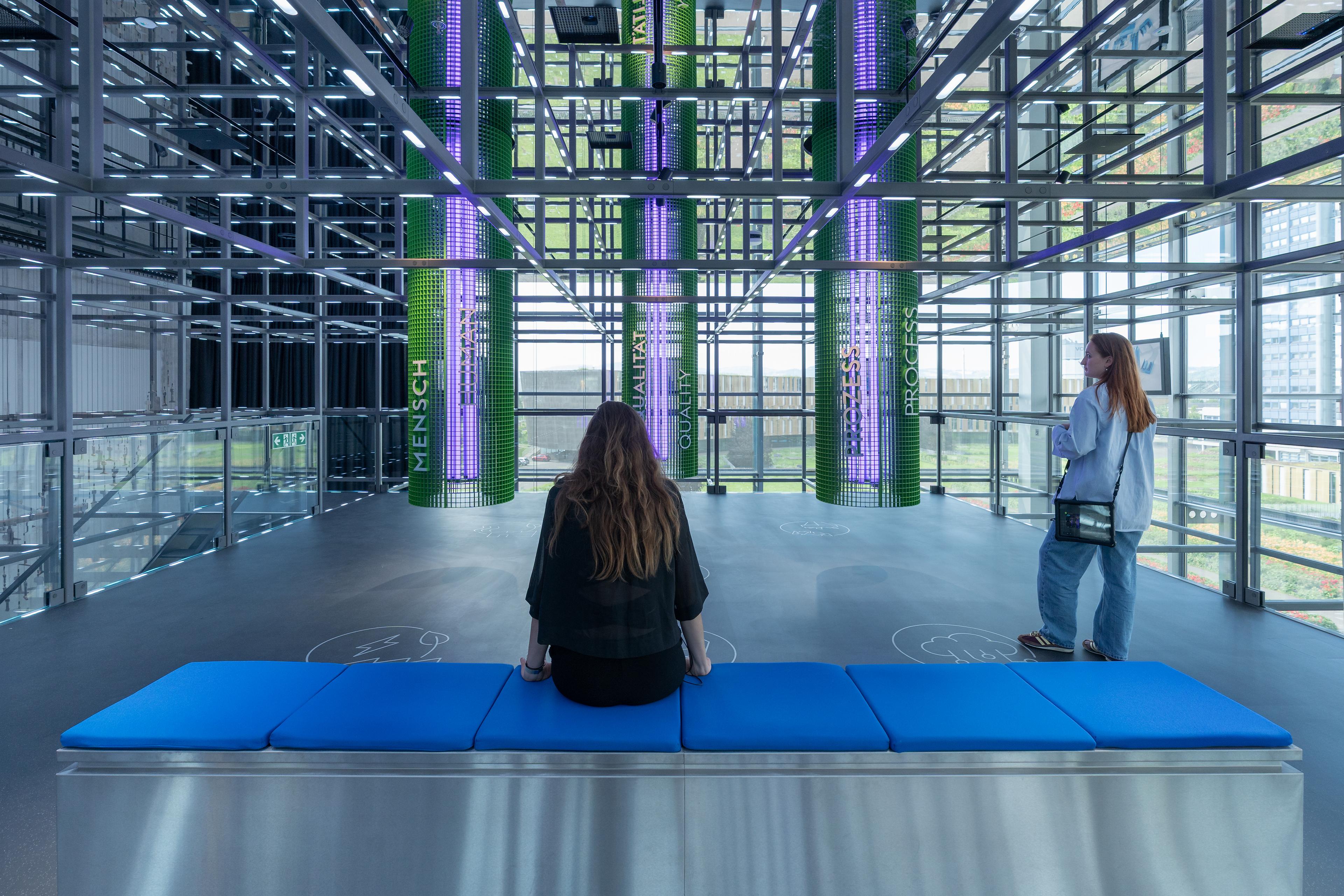Visitors observe an immersive installation within the suspended Grid, where illuminated columns visualize the core values and interconnected processes of voestalpine